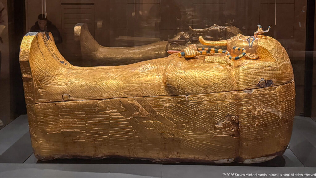 Large gilded anthropoid coffin of Tutankhamun with royal face, crossed regalia, and winged decoration.