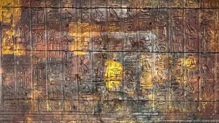 Dark funerary panel with worn hieroglyphs and small figures highlighted in gold, red, yellow, and blue.