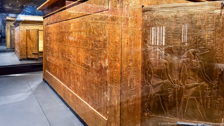 Corner of gilded funerary shrine with hieroglyphic columns, standing deities, and a winged motif.