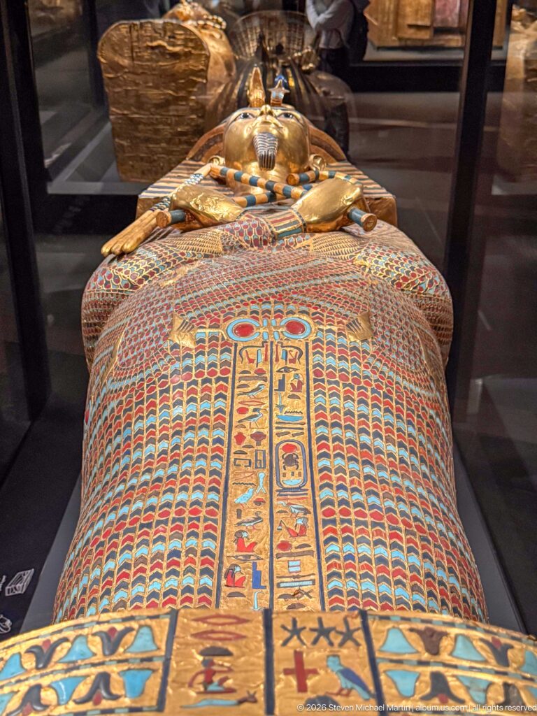 Overhead view of Tutankhamun anthropoid coffin with gilded face, broad colored collar, and hieroglyphic decoration.