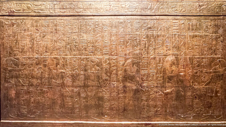 Close gilded panel filled with vertical hieroglyphs and rows of small ritual figures.