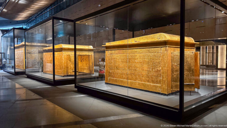 Two large gilded funerary shrines displayed in adjacent glass cases, one broadside and one behind.
