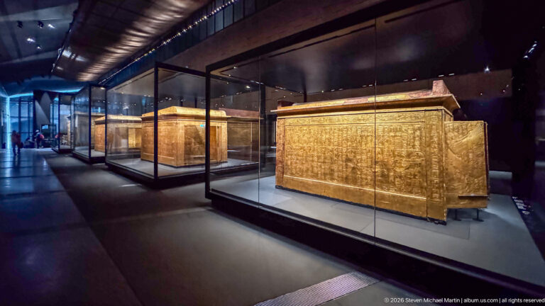 Multiple gilded funerary shrines displayed in a row inside separate glass museum cases.