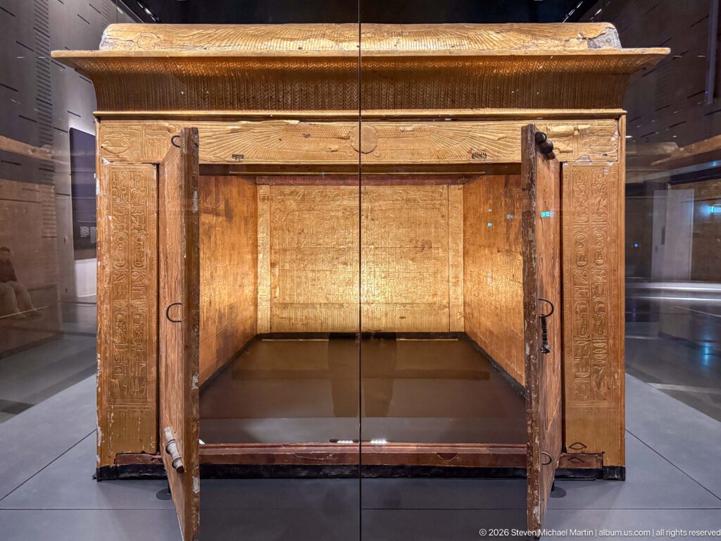 Front view of gilded funerary shrine with two doors opened outward around an empty rectangular cavity.