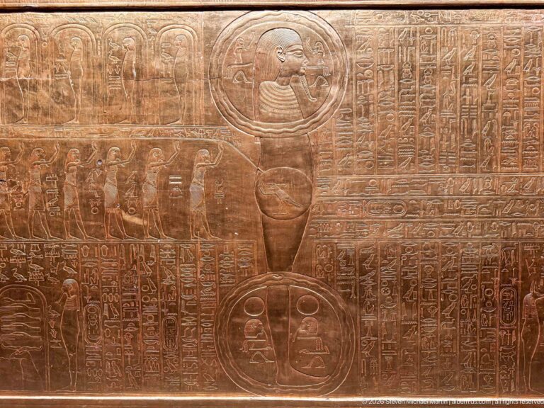 Close gilded panel with hieroglyphs, cartouches, and a profile royal head inside a circular frame.