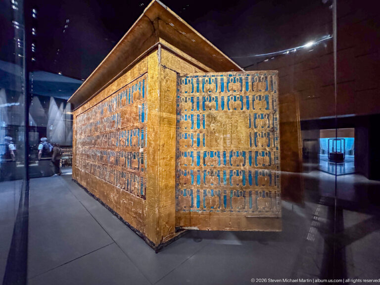 Oblique corner view of a large gilded shrine covered with repeated blue-inlaid motifs.