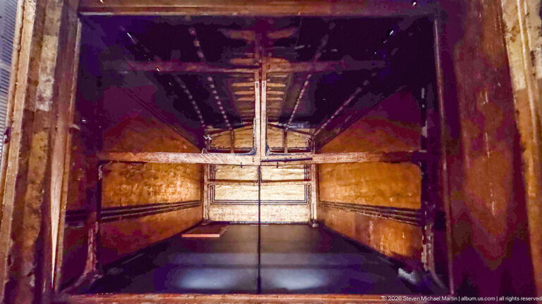 View into the narrow interior chamber of a gilded funerary shrine with a raised roof structure.