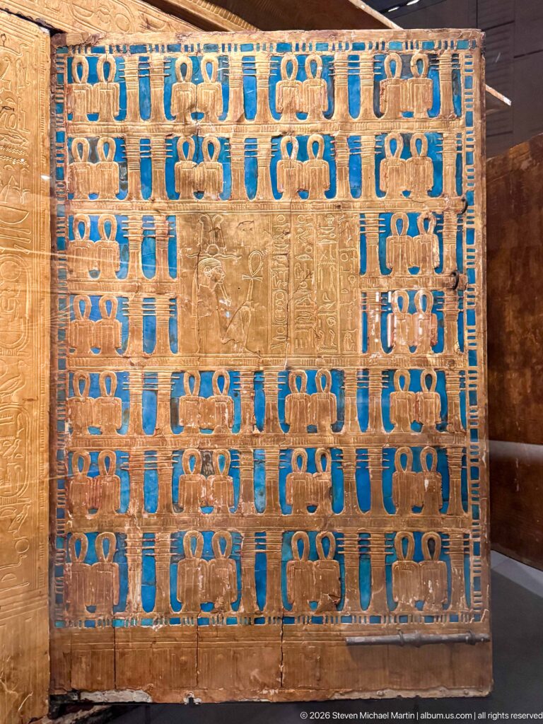Close view of gilded shrine panel with blue inlay framing a central field of hieroglyphs and figures.