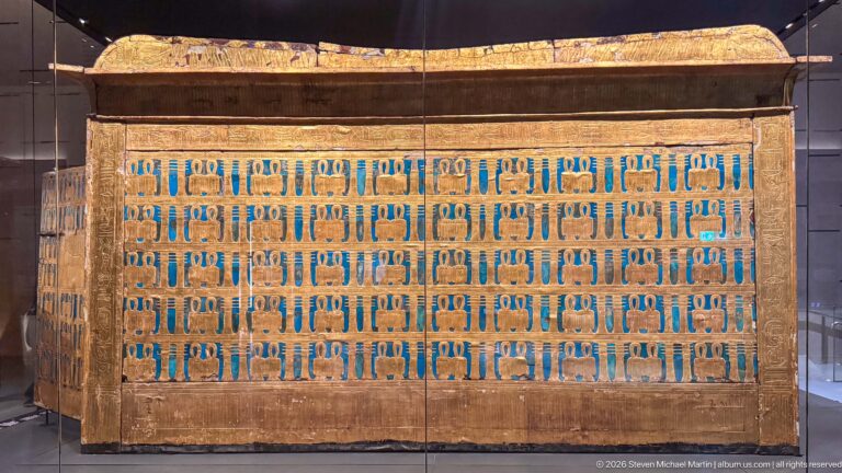 Large gilded funerary shrine with rows of blue-inlaid protective motifs and a projecting upper cornice.