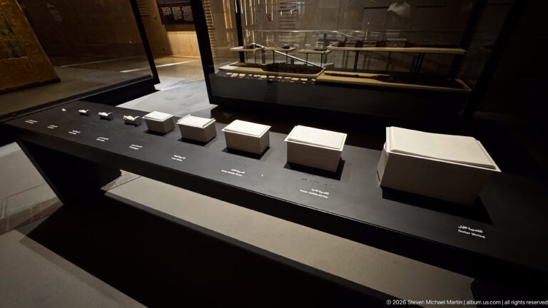 Graduated white rectangular boxes or containers arranged in a row on a black museum display.