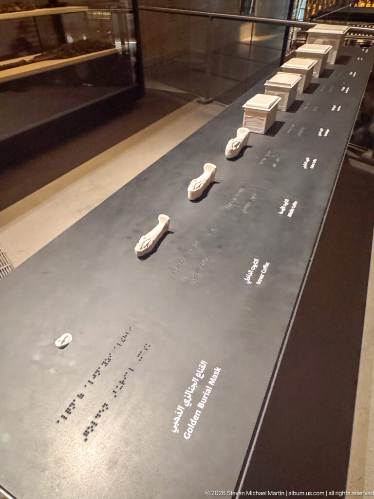 Row of small pale artifacts displayed individually along a long black museum plinth.