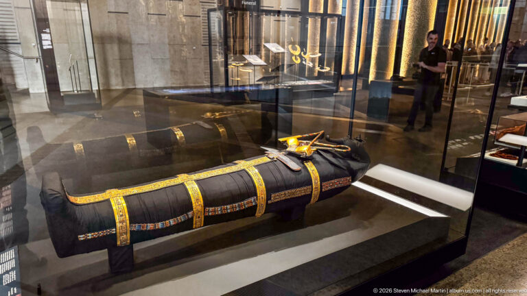 Full side view of black wrapped anthropoid form with repeated gold bands and colorful edging.