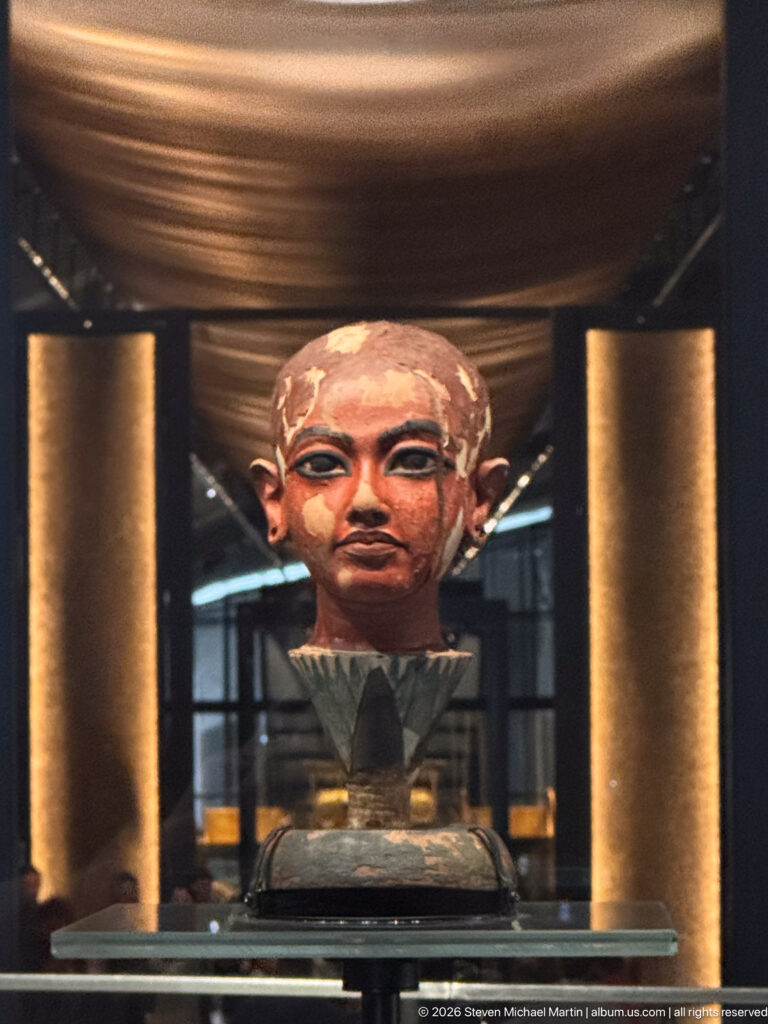 Close frontal view of painted Tutankhamun bust framed by tall illuminated museum columns.