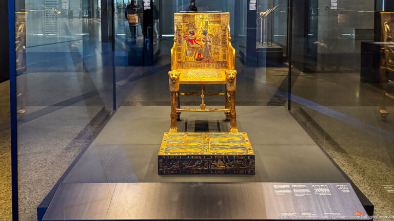 Tutankhamun’s Golden Throne and footstool centered at the end of a long glass display case.