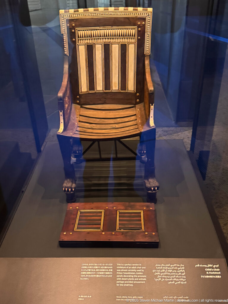 Decorated wooden chair with striped rectangular back, curved slatted seat, side supports, and footboard.