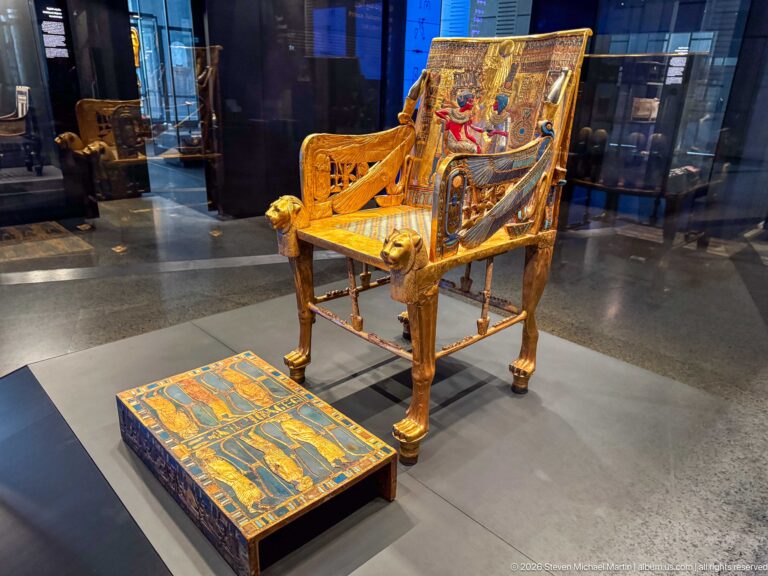 Complete Golden Throne of Tutankhamun with decorated royal-couple backrest, gilded side panels, and footstool.