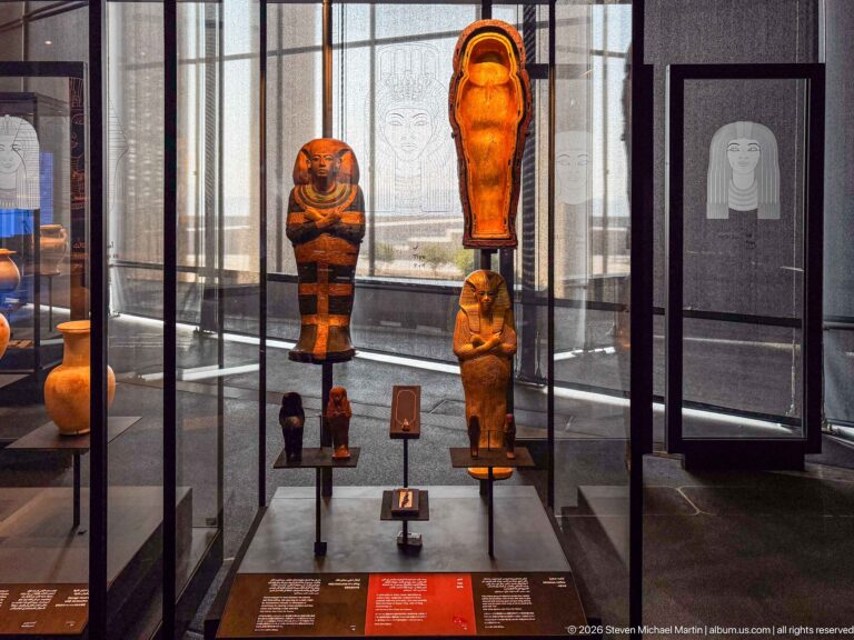 Glass case with multiple funerary statuettes and mummiform figures of different sizes and colors.