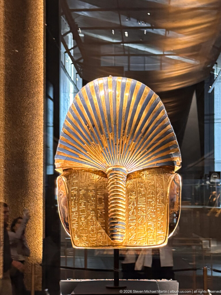 Rear of Tutankhamun’s solid-gold burial mask with blue-and-gold nemes stripes and protective hieroglyphic inscription.