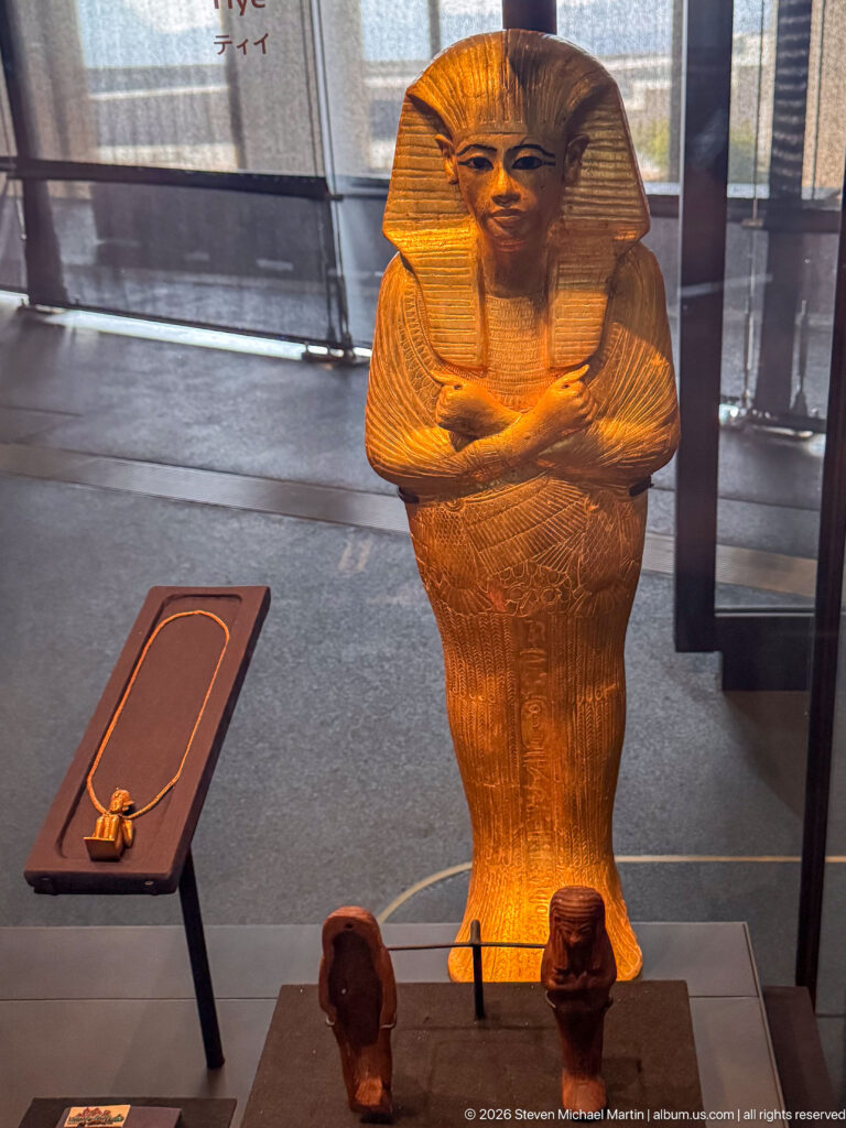 Large mummiform figure with striped headdress, crossed arms, and warm gold-brown surface.