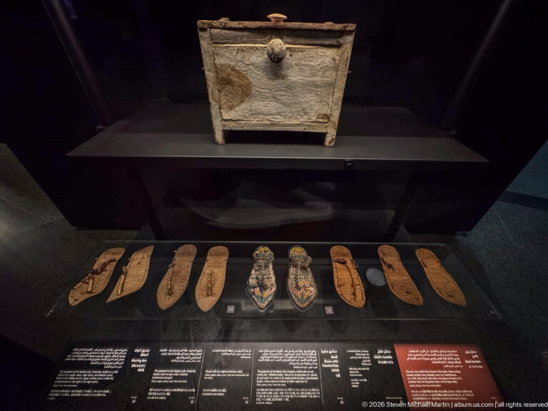 Small chest above a row of ancient sandals, including two richly decorated blue-and-gold pairs.
