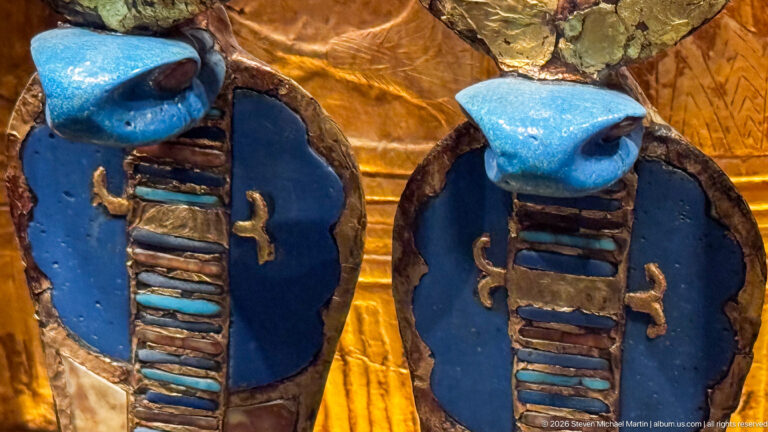 Close pair of vivid blue scarab-like ornaments with striped central bodies set against a gilded surface.