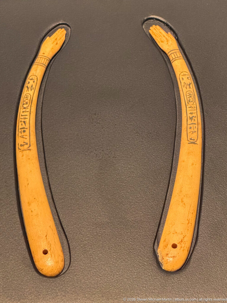 Pair of pale crescent-shaped inscribed objects with tapered tips and small holes near the broader ends.
