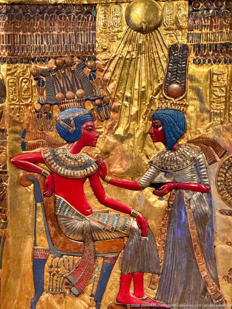 Close throne-back scene of Tutankhamun and Ankhesenamun beneath the radiating Aten disk and floral canopy.