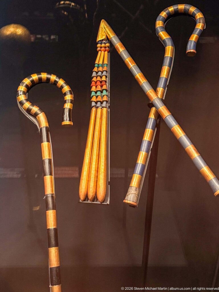 Striped ceremonial staffs and crooks with alternating gold, blue, red, and dark bands displayed together.