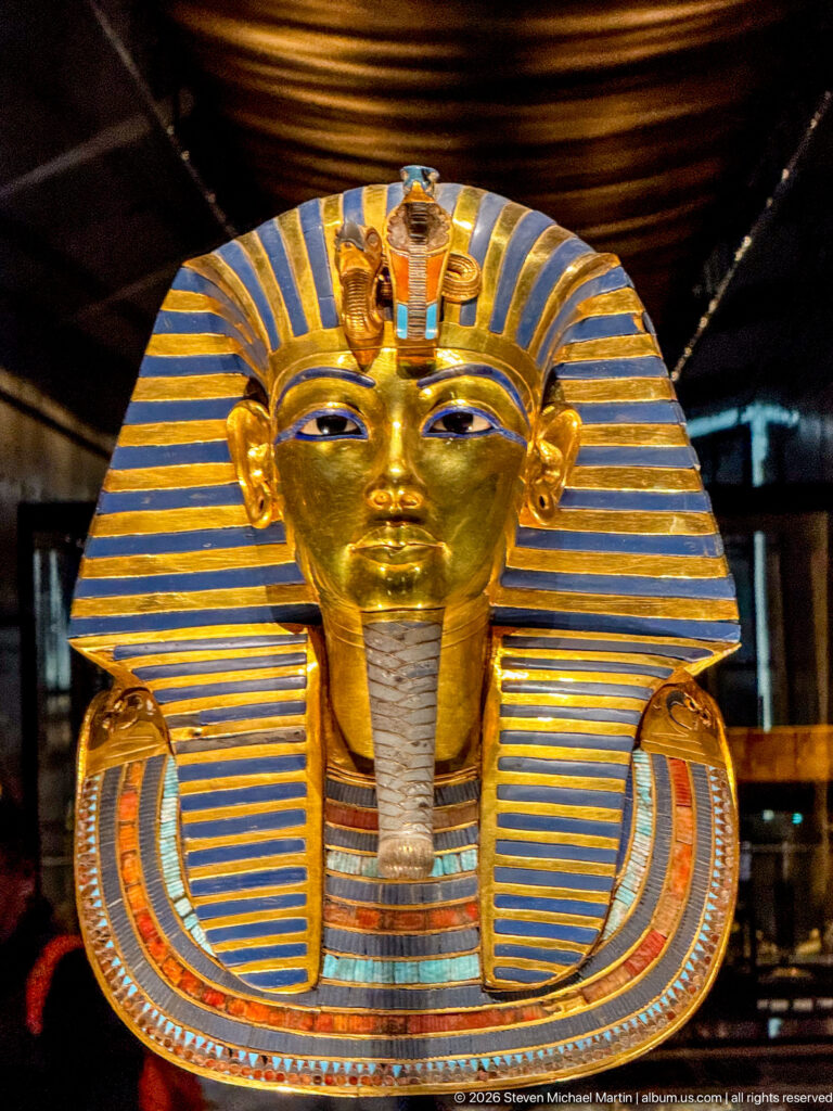Frontal close view of Tutankhamun’s solid-gold burial mask with striped nemes, brow emblems, false beard, and inlaid collar.