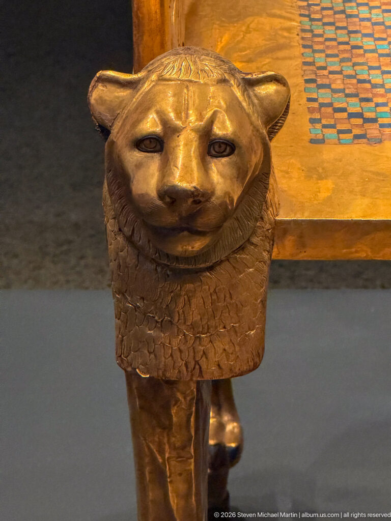 Close gilded lion head with textured mane attached to a vertical furniture support.