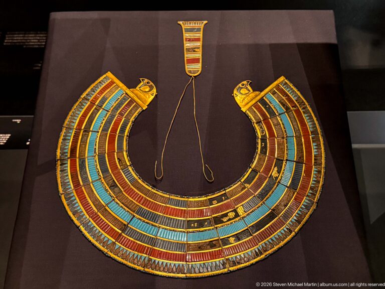 Broad multicolored collar with falcon-head terminals and thin cords rising to a rectangular clasp.