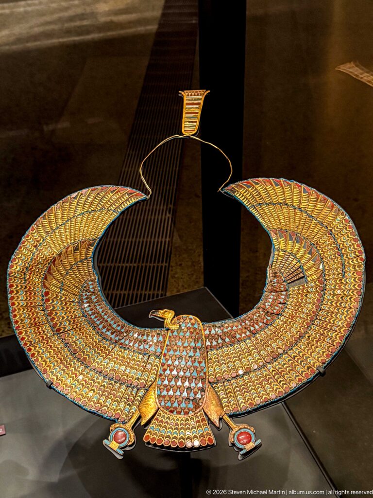 Frontal view of multicolored winged falcon pectoral with body centered below broad curved wings.
