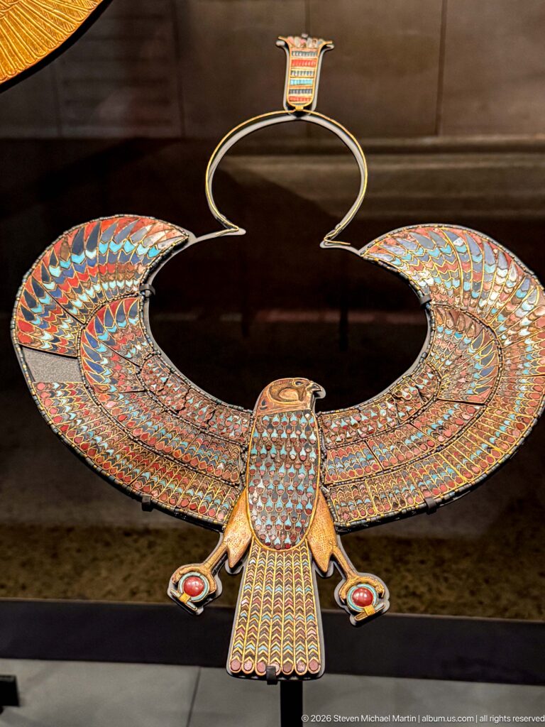 Large winged falcon pectoral with multicolored inlay, patterned body, and suspension loop above.