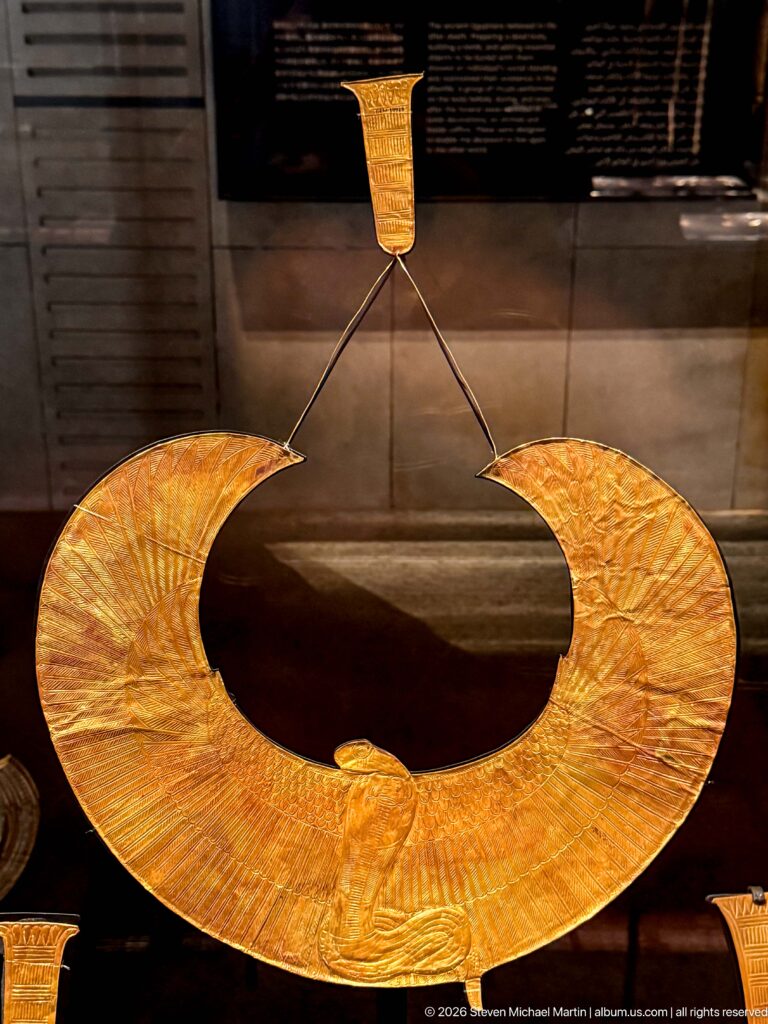 Large semicircular gold collar with fine radiating engraved lines and thin suspension cords.