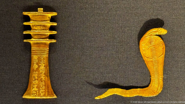 Gold rearing cobra ornament with expanded hood and long curved body on a dark display surface.