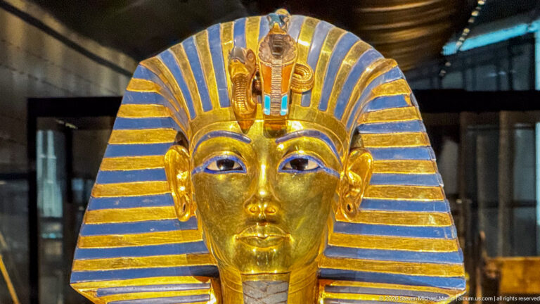Frontal close view of Tutankhamun’s solid-gold burial mask with striped nemes, brow emblems, false beard, and inlaid collar.