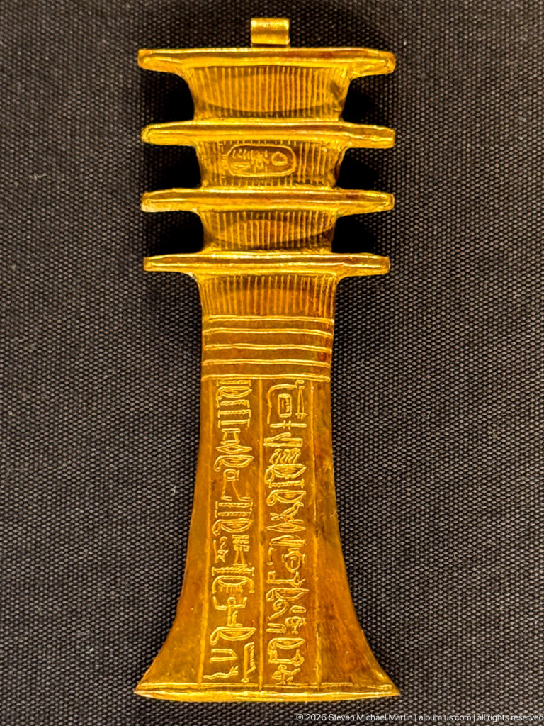 Tall gold stand with flared inscribed base and several stacked projecting platforms at the top.