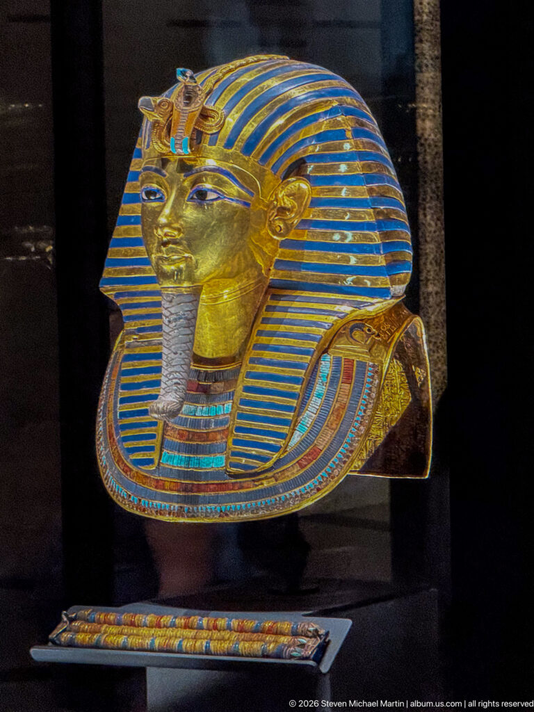 Frontal close view of Tutankhamun’s solid-gold burial mask with striped nemes, brow emblems, false beard, and inlaid collar.