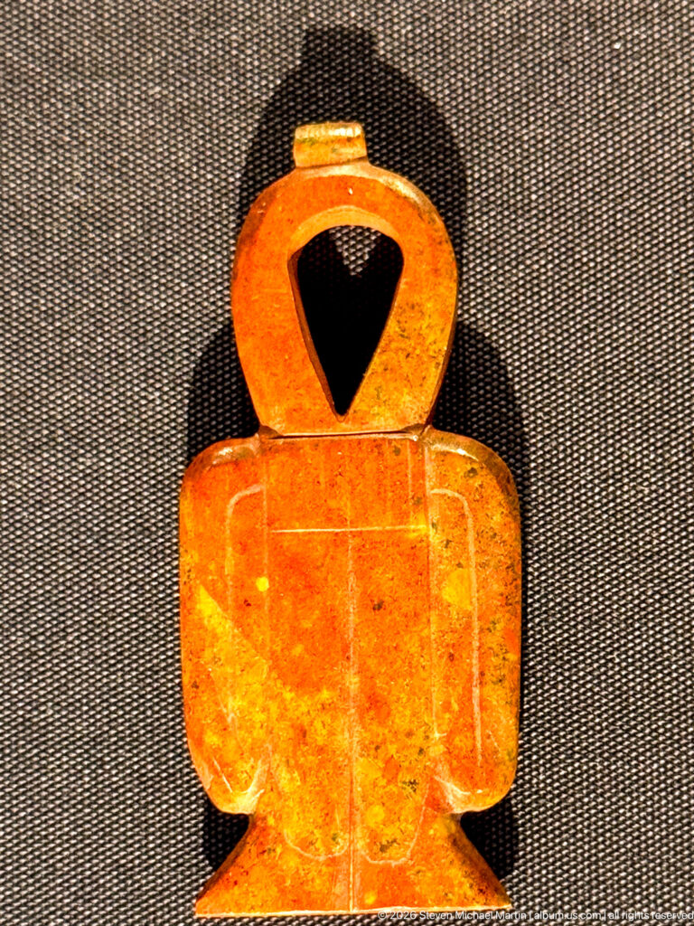 Gold ornament with broad rectangular lower body and large circular suspension loop above.