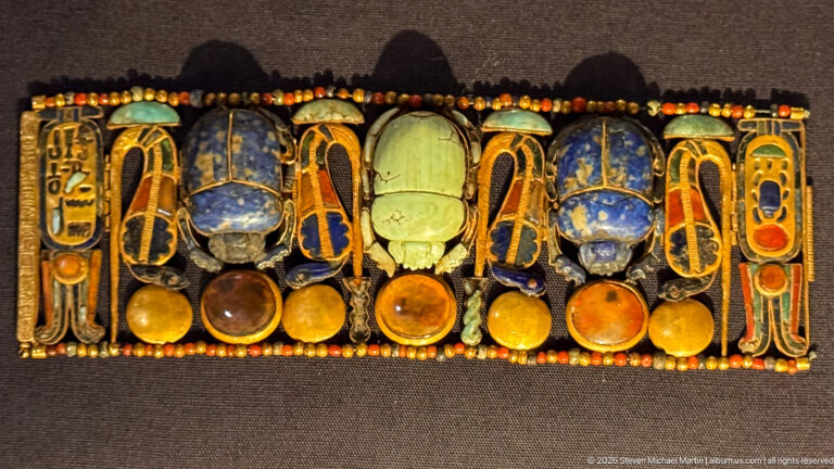 Elaborate jeweled pectoral with blue and green scarabs, gold framing, cartouches, and round disk elements.