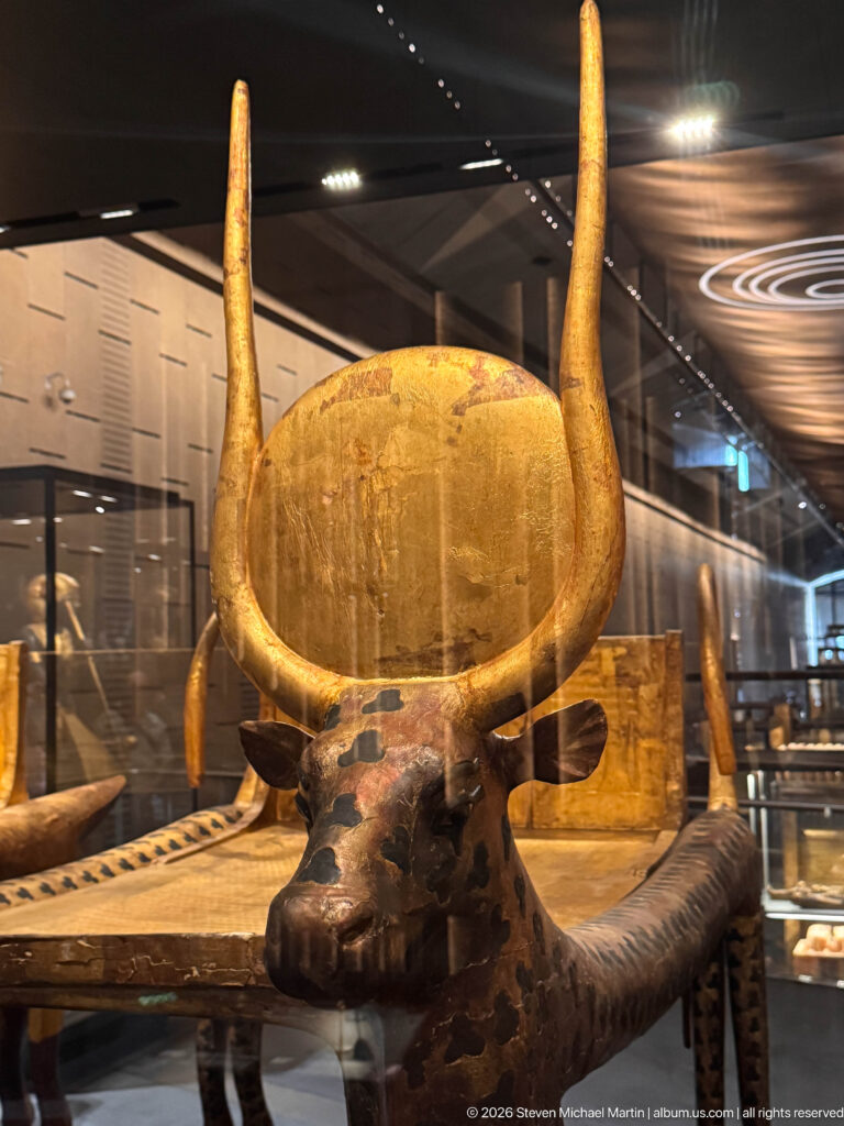 Front view of a funerary couch with bovine head, tall horns, and a large circular element behind.