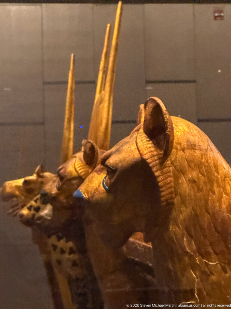 Close side view of a gold-toned animal head with long muzzle, painted eye, and two tall upright projections.