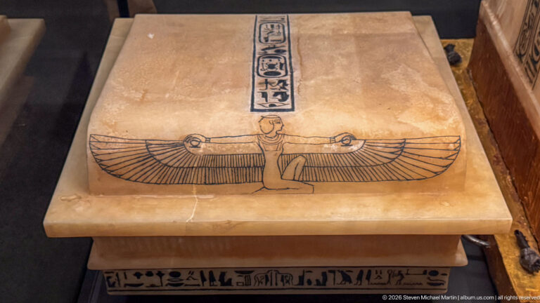 Pale stone panel with a kneeling winged goddess and vertical royal inscription above her.
