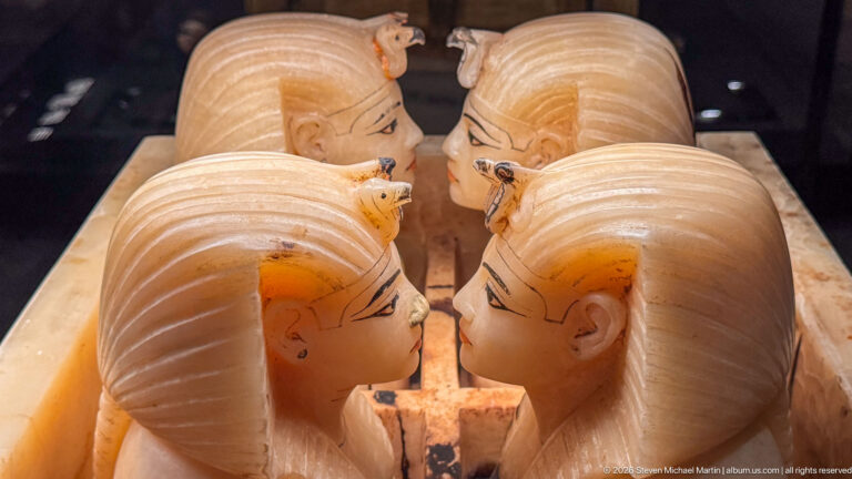Four travertine royal-head stoppers from Tutankhamun’s canopic chest arranged in facing pairs with painted facial details.