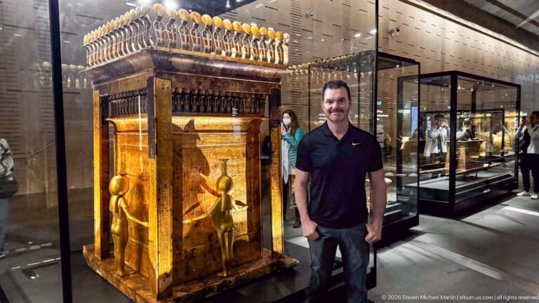 Tutankhamun’s gilded Canopic Shrine on a Sledge with protective goddesses and a visitor beside it for scale.