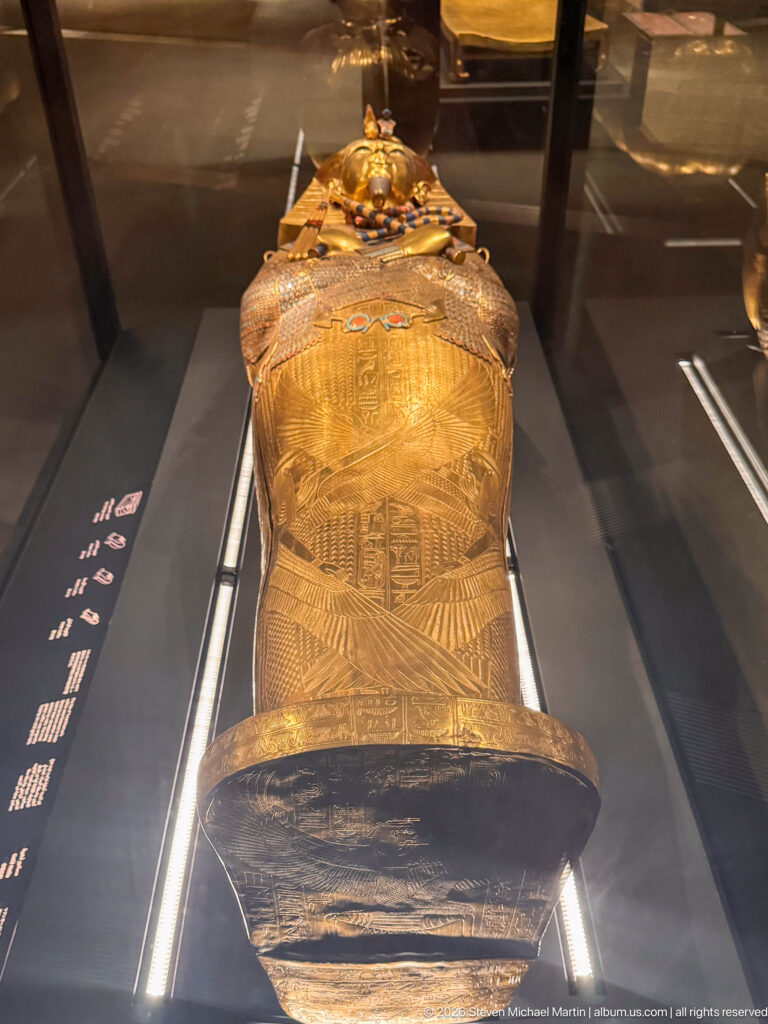 Foot-end view along a decorated anthropoid coffin with winged motifs and hieroglyphic bands.