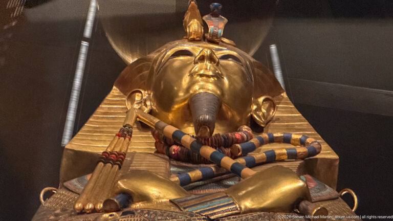 Close gilded royal coffin face with striped headdress, crossed regalia, and colored inlay.