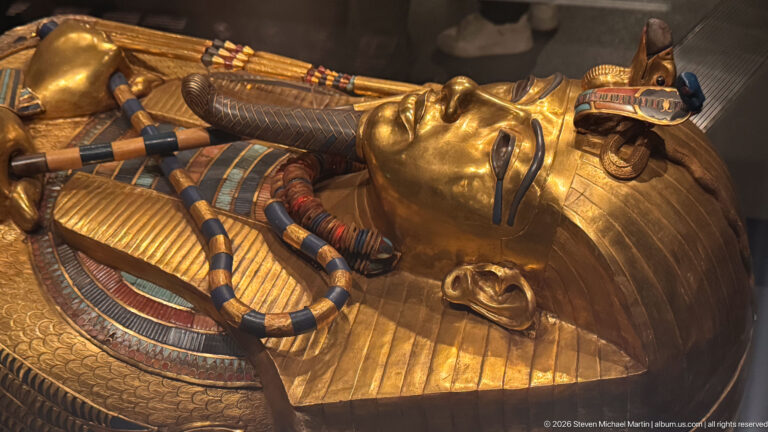 Upper body of gilded Tutankhamun coffin with crossed crook and flail, broad collar, and royal face.