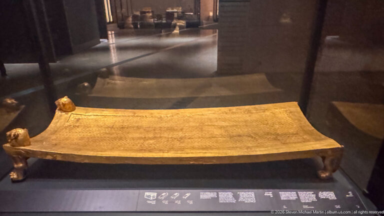 Low gilded funerary bed or bier with a gently curved surface and small animal-form supports.