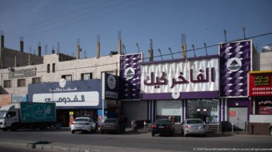 Purple-and-white Arabic furniture storefront with parked cars and an unfinished building structure rising behind it.